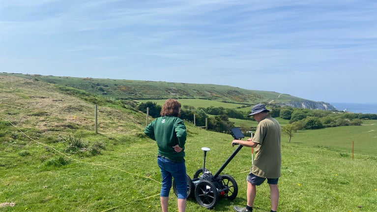 Two people with back to camera using surveying equipment on green grassy area